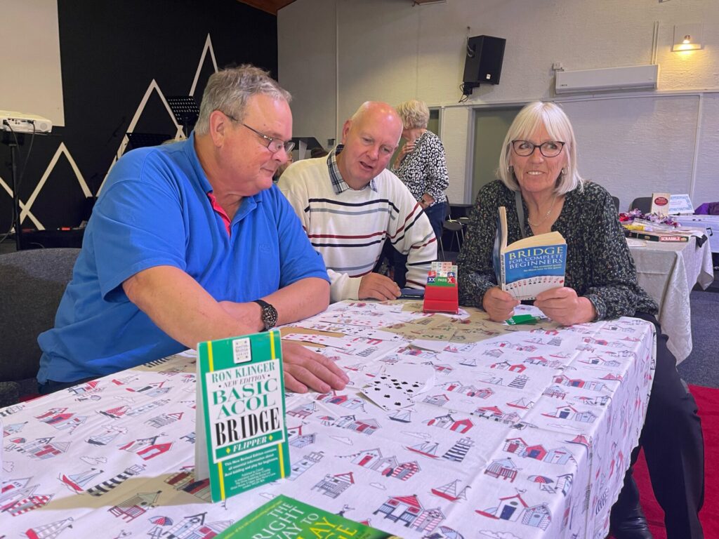 2 men and 1 woman at a table with books and playing cards.